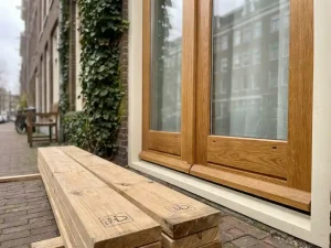 Nieuw geplaatst houten kozijn van FSC-gecertificeerd eikenhout in Nederlandse gevel met HR++-glas en klimopbeklede bakstenen muur.