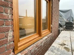 Nieuw geplaatst meranti houten kozijn in bakstenen gevel tijdens renovatie, met HR++ glas en steiger op de achtergrond.