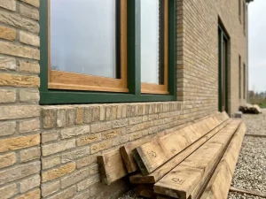 Houten kozijn met zichtbare eikenhoutnerf in nieuwbouw gevel van Nederlandse baksteen, FSC-gecertificeerde planken eronder.